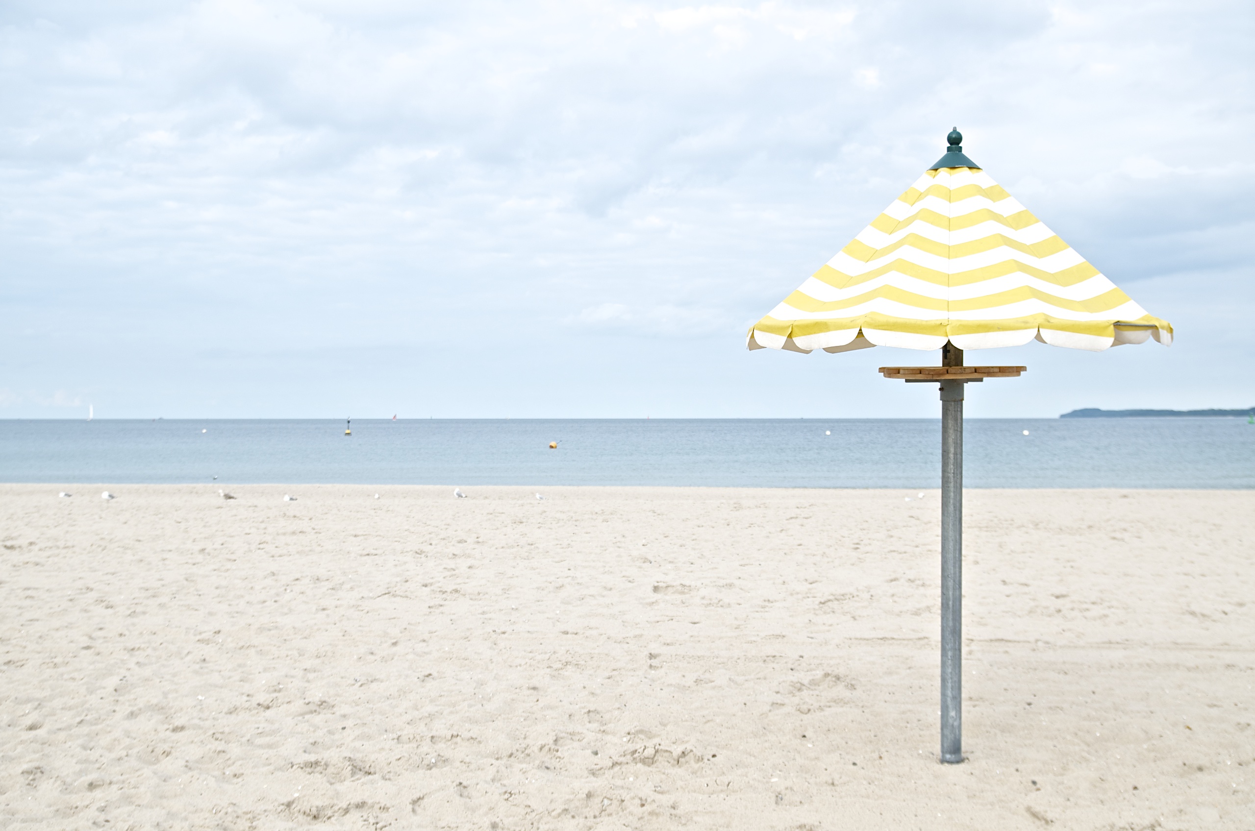 (K)Ein Tag am Meer,gelb-weiß gestreifter Sonnenschirm am Strand in Travemünde, Himmel, Meer